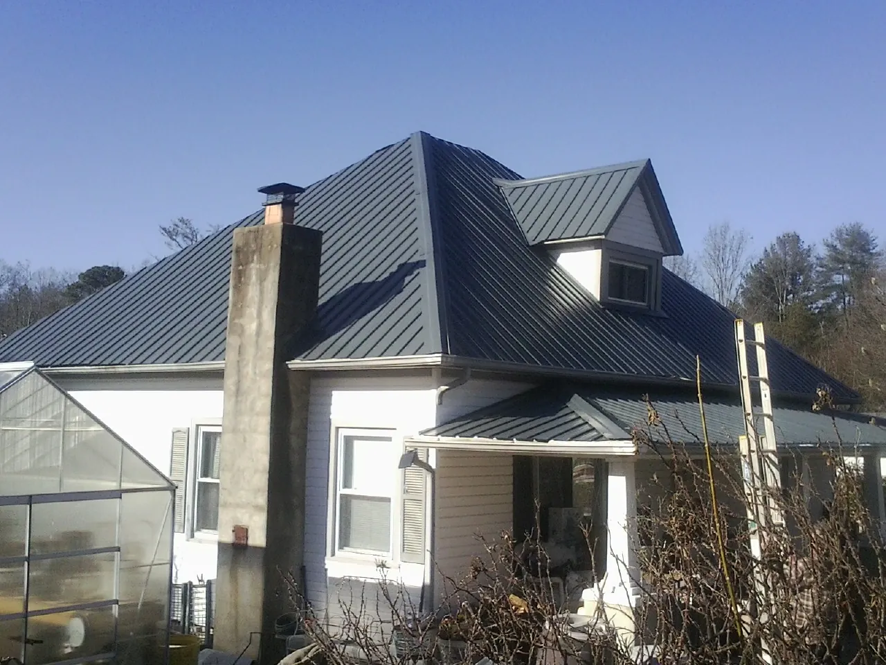 Dark blue standing seam metal roof on a white farmhouse with dormer — Slate & Tile Roof Repair by Roofing Brothers in Argusville