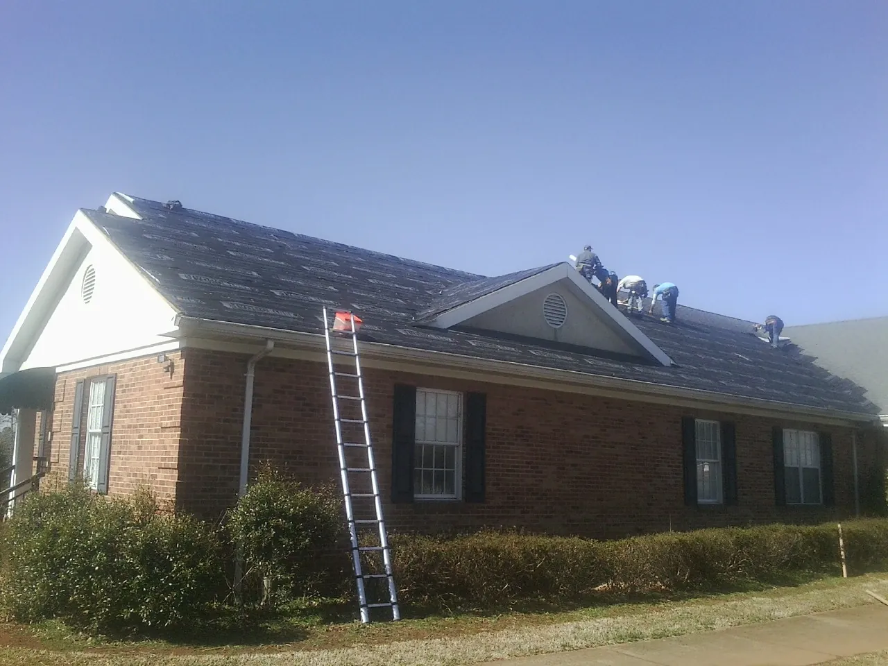 Crew tearing shingles off a brick ranch roof with a ladder set — Metal Roof Repair work by our crew in Argusville