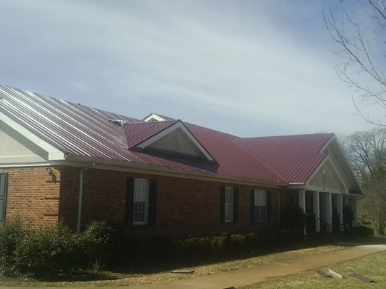 Red metal roof with gabled entries on a long brick building, from a Hail Damage Roof Repair job in Argusville