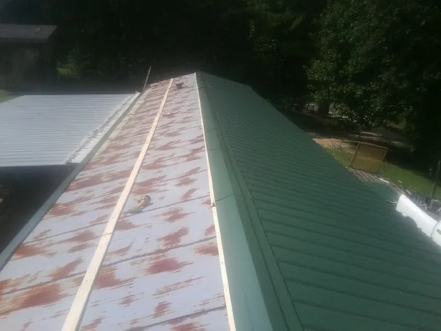 Old rusted panels beside newly installed green metal roofing — Wind Damage Roof Repair by Roofing Brothers in Argusville