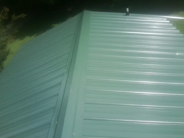 New green metal panels meeting at the ridge of a roof — Flat Roof Repair work by our crew in Argusville