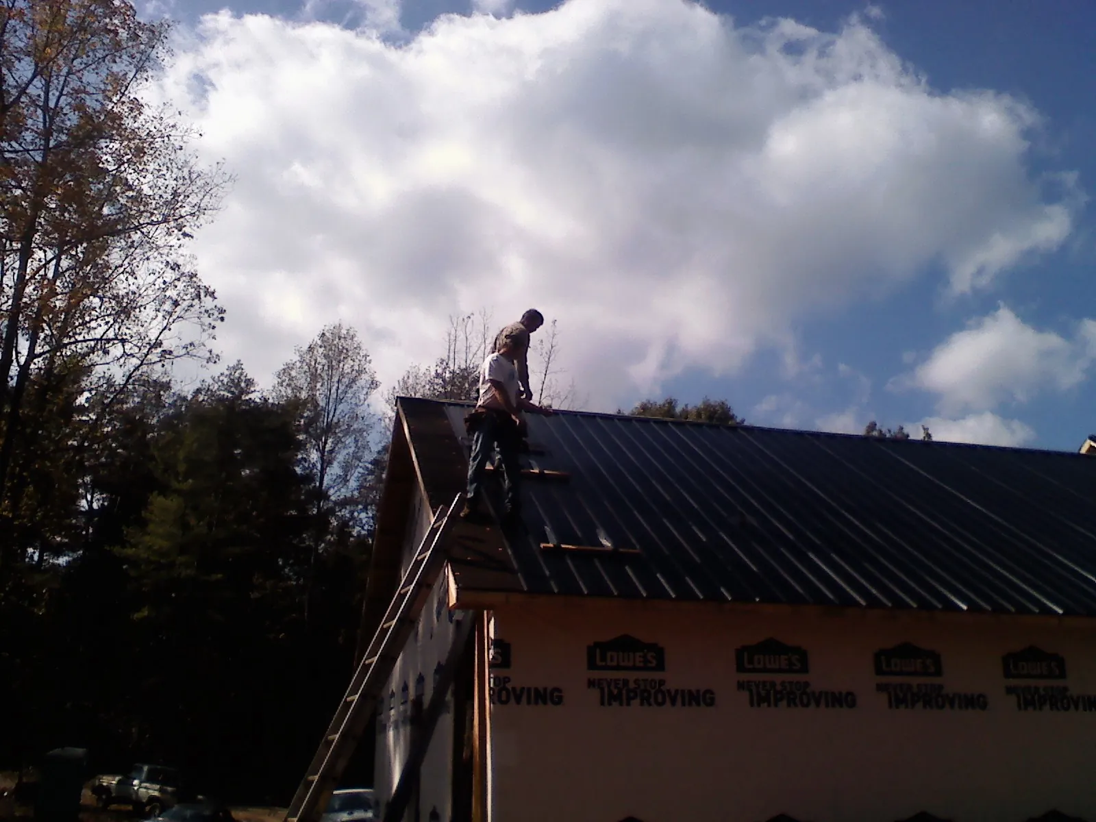 Roofer fastening dark metal panels high against a cloudy sky, from a Roof Inspection job in Argusville