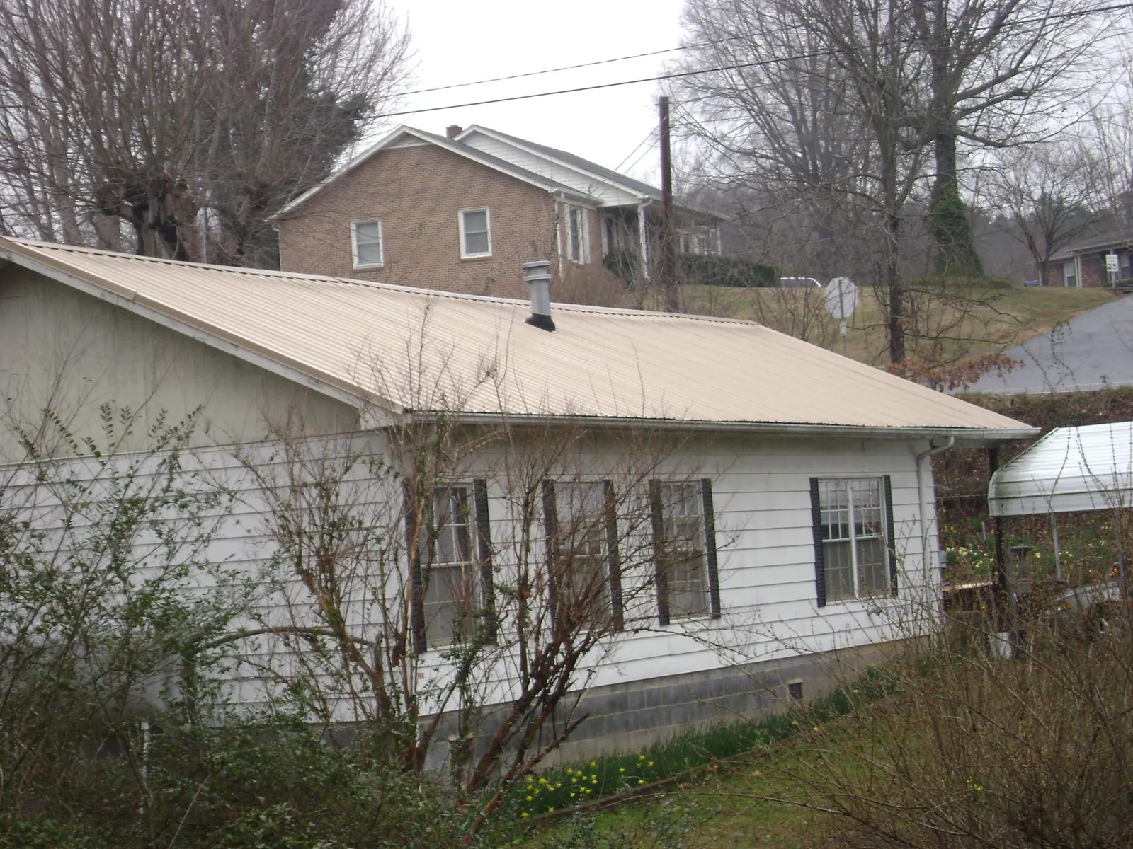 Tan metal roof on a white sided house set into a hillside — Commercial Roofing by Roofing Brothers in Argusville